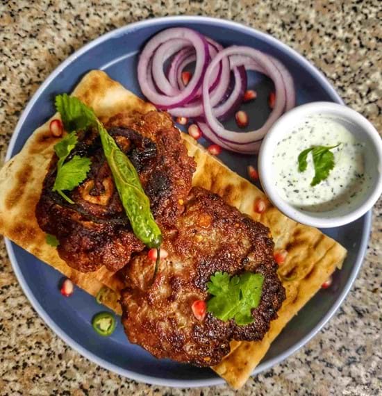 Lamb Chapli Kebabs: A Flavourful Fusion Delight Chapli Kebabs on a blue plate served with red onions
